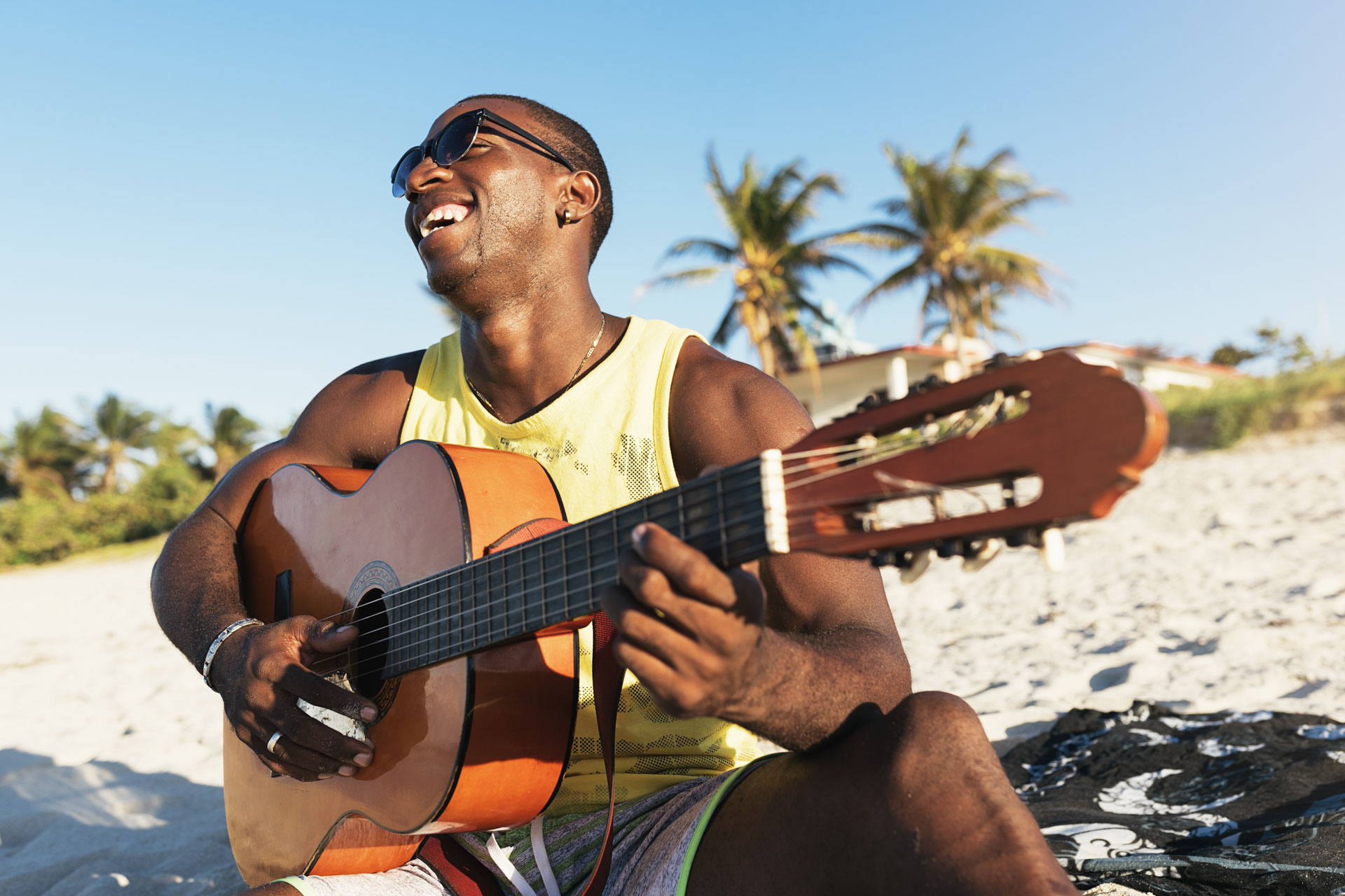 Young cuban man having fun in the beach with his guitar. Friendship concept.